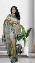 Woman wearing a traditional pure katan silk saree with a green and beige pattern in a modern indoor setting.