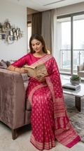 Woman in a pink pure Katan Silk saree reading a book in a modern living room.