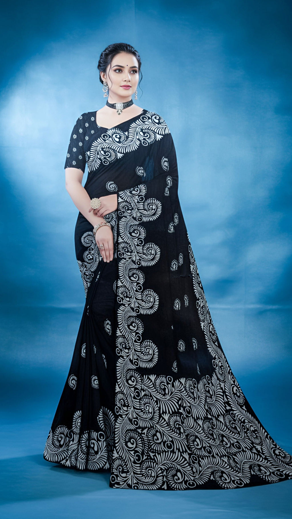 Woman wearing a black saree with white alpona paint, against a light background