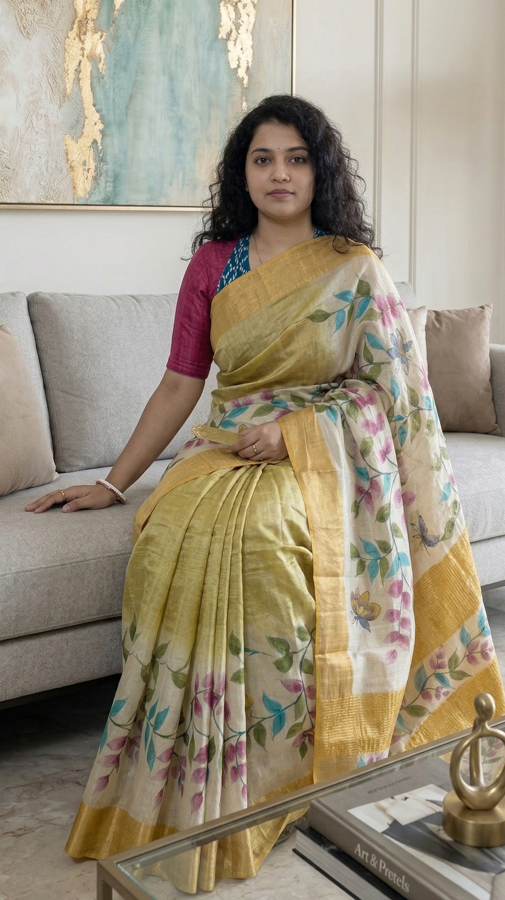 Woman in a yellow saree with floral patterns sitting on a couch in a living room.