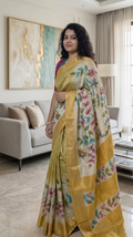 Woman in a yellow saree with floral patterns standing in a modern living room.