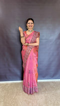 Woman in a pink katan silk saree standing against a plain background