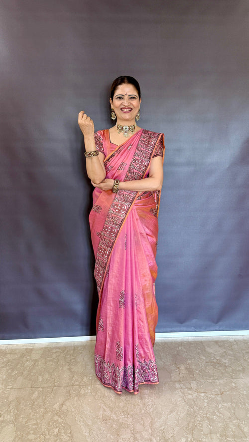 Woman in a pink katan silk saree standing against a plain background