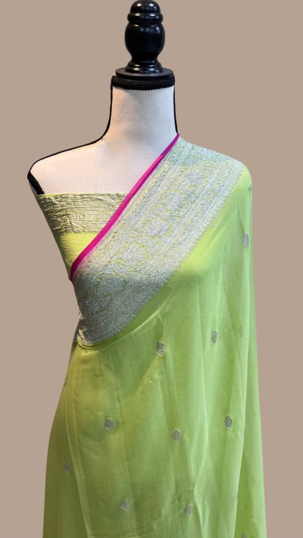 A light green saree with a silver embroidered blouse and a bright pink border, displayed on a mannequin torso against a solid beige background.
