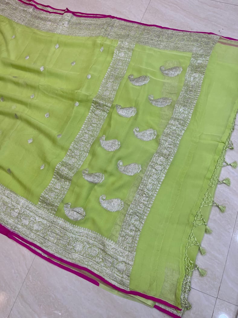 A lime green saree or sari with silver paisley and floral embroidery, featuring a wide metallic border and magenta pink edges, laid flat on a light-colored tiled floor.