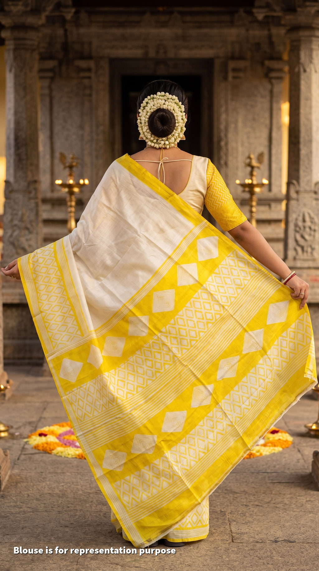 A woman wearing a yellow and white saree is shown from behind, standing in front of a stone temple structure with brass oil lamps. The text 'Blouse is for representation purpose' is visible at the bottom left.